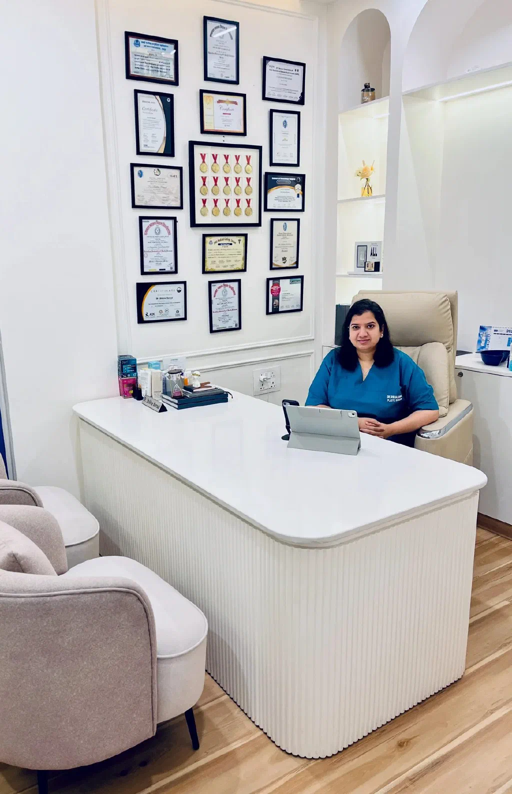 Dr. Shikha Bansal at her desk in the white consultation room, certificates on the wall behind her